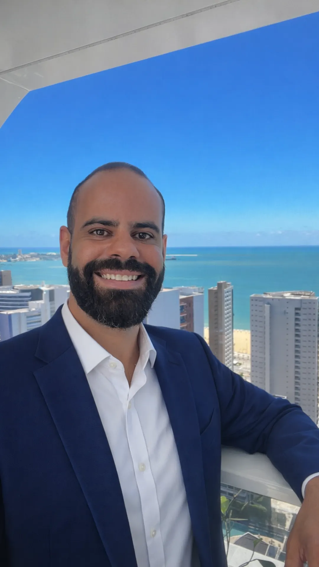 Selfie do fundador da ROTNA de blazer azul, sorrindo, com prédios e o mar ao fundo.
